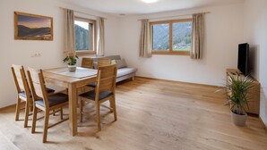 A room with a dining table, chairs, a sofa, a TV, and a window with curtains. - Apartment "Radlspitz - Maurerhof" with Mountain View, Wi-Fi & Garden (Sarntal - Südtirol (BZ))