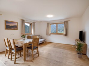 A room with a dining table, chairs, a sofa, a TV, and a window with curtains.
