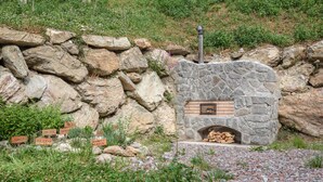 A stone-built outdoor fireplace with firewood stored inside, surrounded by a rocky landscape and greenery. - Apartment "Radlspitz - Maurerhof" with Mountain View, Wi-Fi & Garden (Sarntal - Südtirol (BZ))