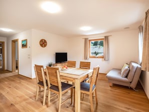 A dining area with a wooden table and chairs, a television, and a window with curtains.