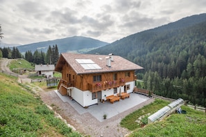 A chalet with a sloped roof, wooden balcony, and a patio area with outdoor furniture.