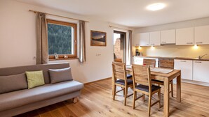 Un salón acogedor con sofá, una mesa de comedor con sillas, una zona de cocina con armarios y una ventana con cortinas.