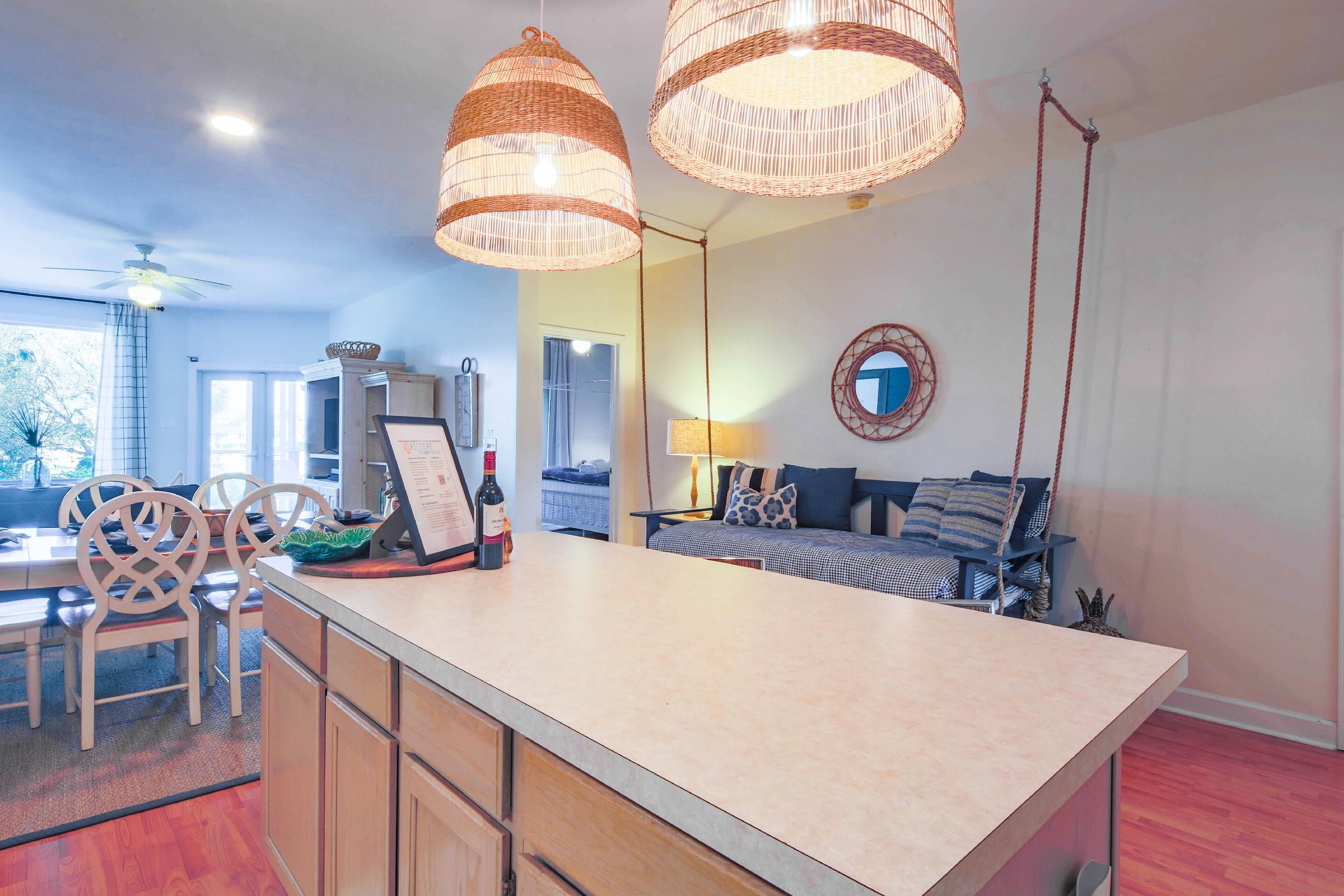 Cocina con isla central, armarios de madera y luces colgantes. Hay un comedor con sillas y una mesa.