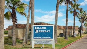 A sign for Island Retreat, a beachfront condominium complex, with palm trees and a clear sky in the background.