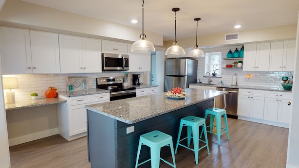 A modern kitchen with white cabinets, granite countertops, stainless steel appliances, and teal bar stools.