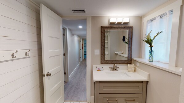 Un bagno con un vanità bianca, uno specchio con cornice decorativa e una finestra con una pianta.