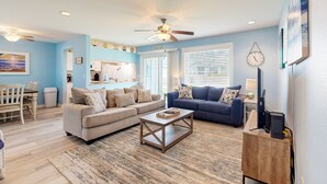 A living room with a beige sectional sofa, a blue sofa, a wooden coffee table, and a dining area with a wooden table and chairs. - 1st Floor, Near Ferry ,Shared Pool, Golf Cart Access (Port Aransas)
