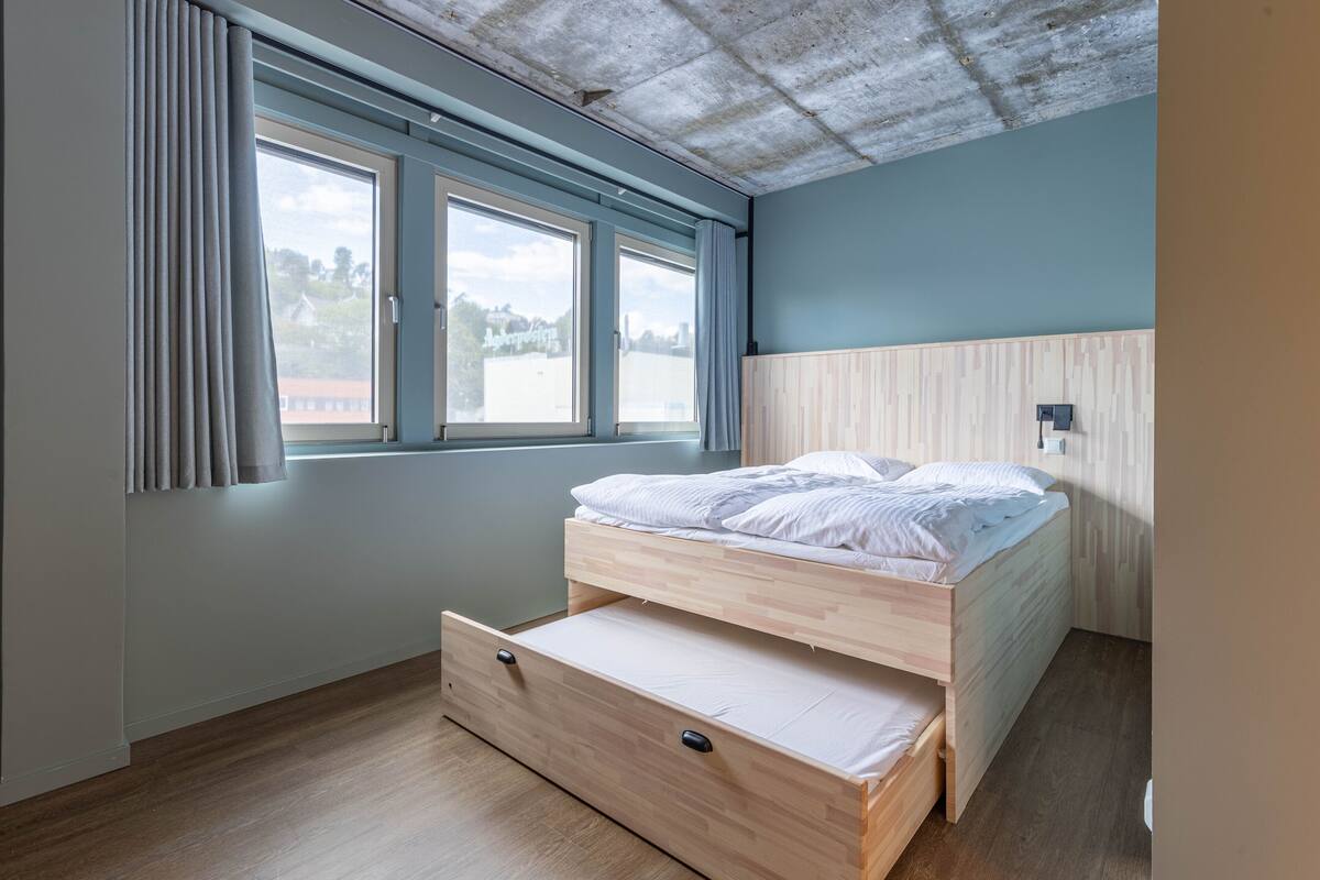 Quarto com cama de madeira, janela com cortinas e vista para o exterior.