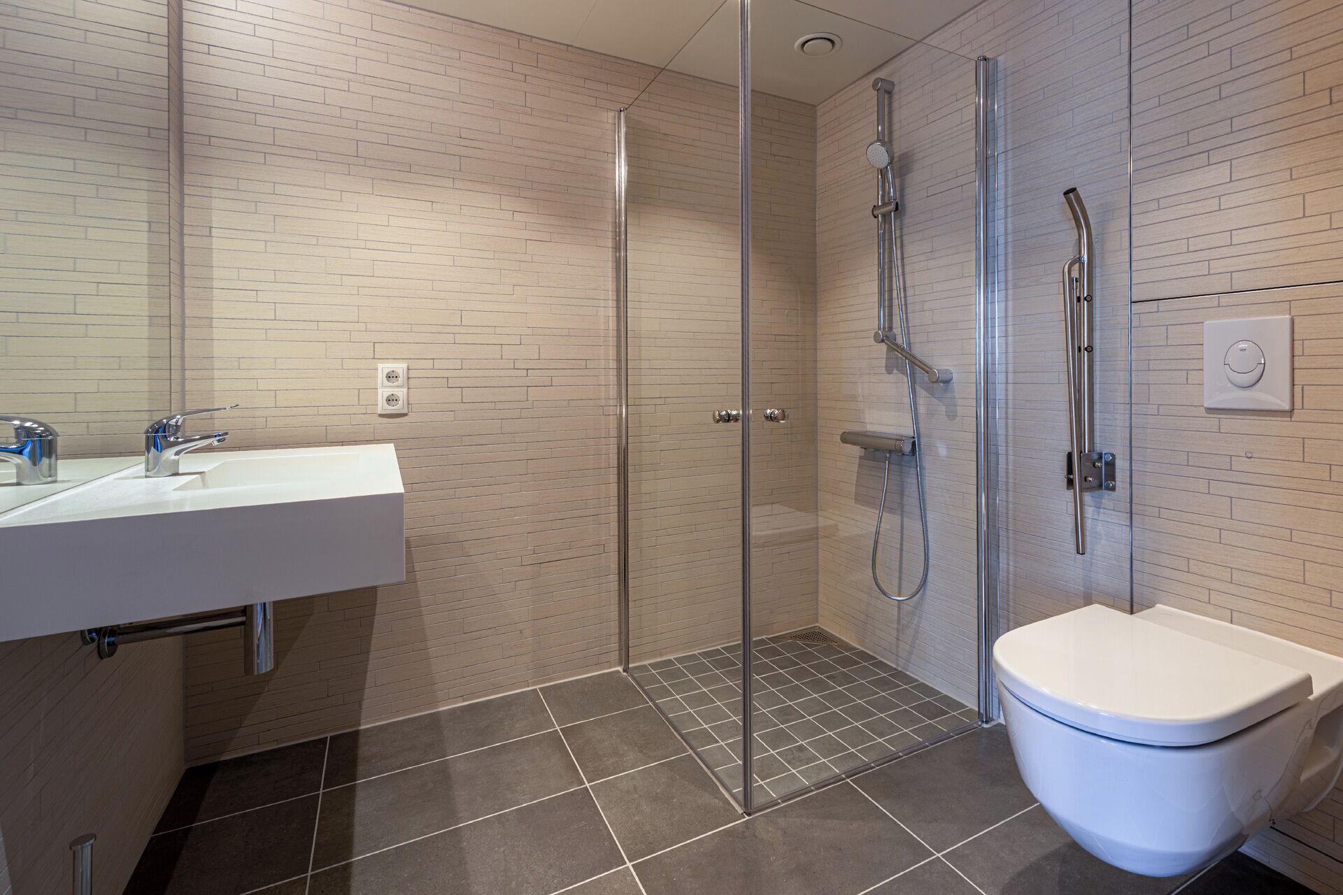 Un baño moderno con cabina de ducha de vidrio, un lavabo blanco y un inodoro.