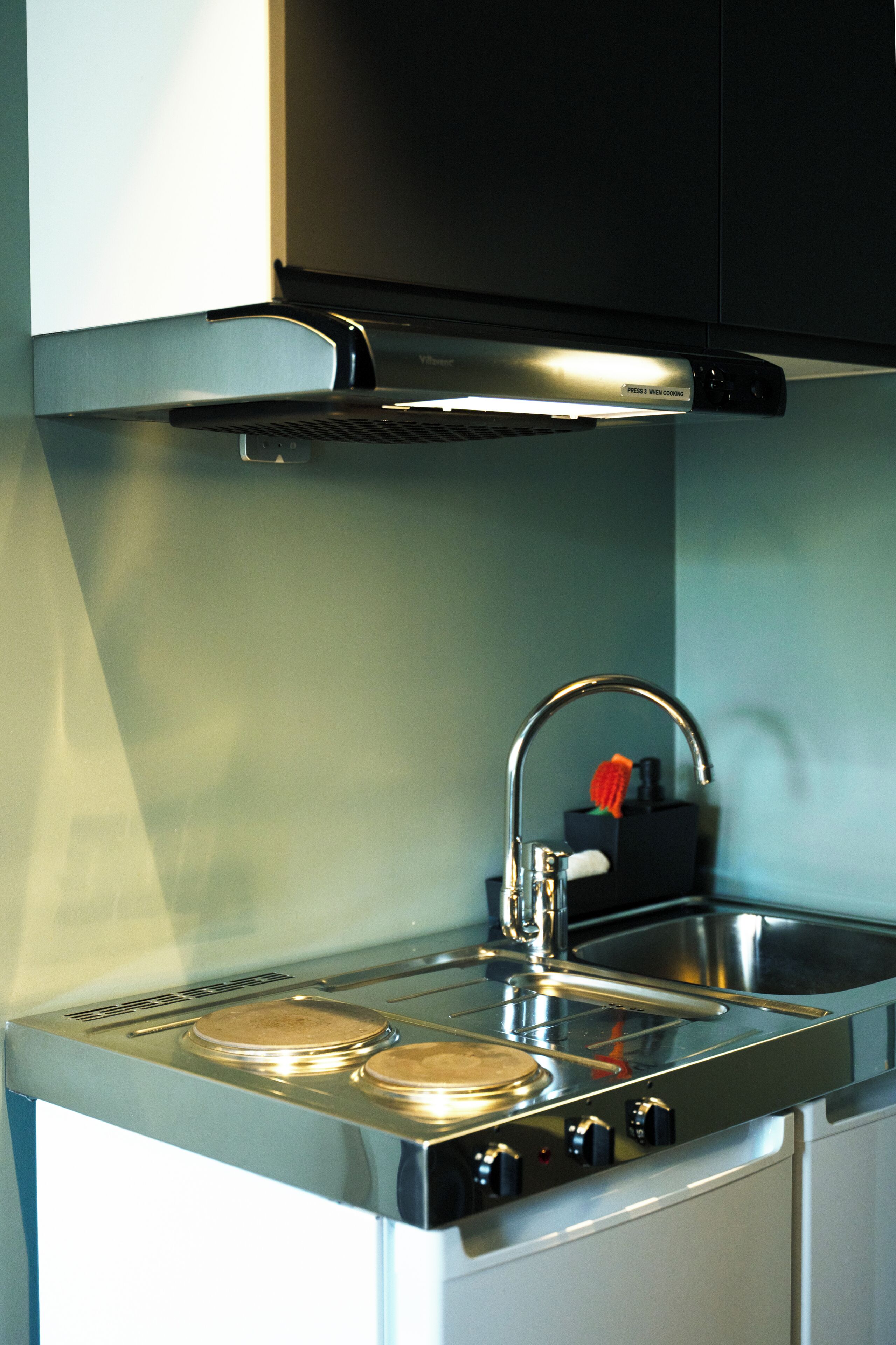 Una cocina compacta con estufa de acero inoxidable, un lavamanos y un grifo.