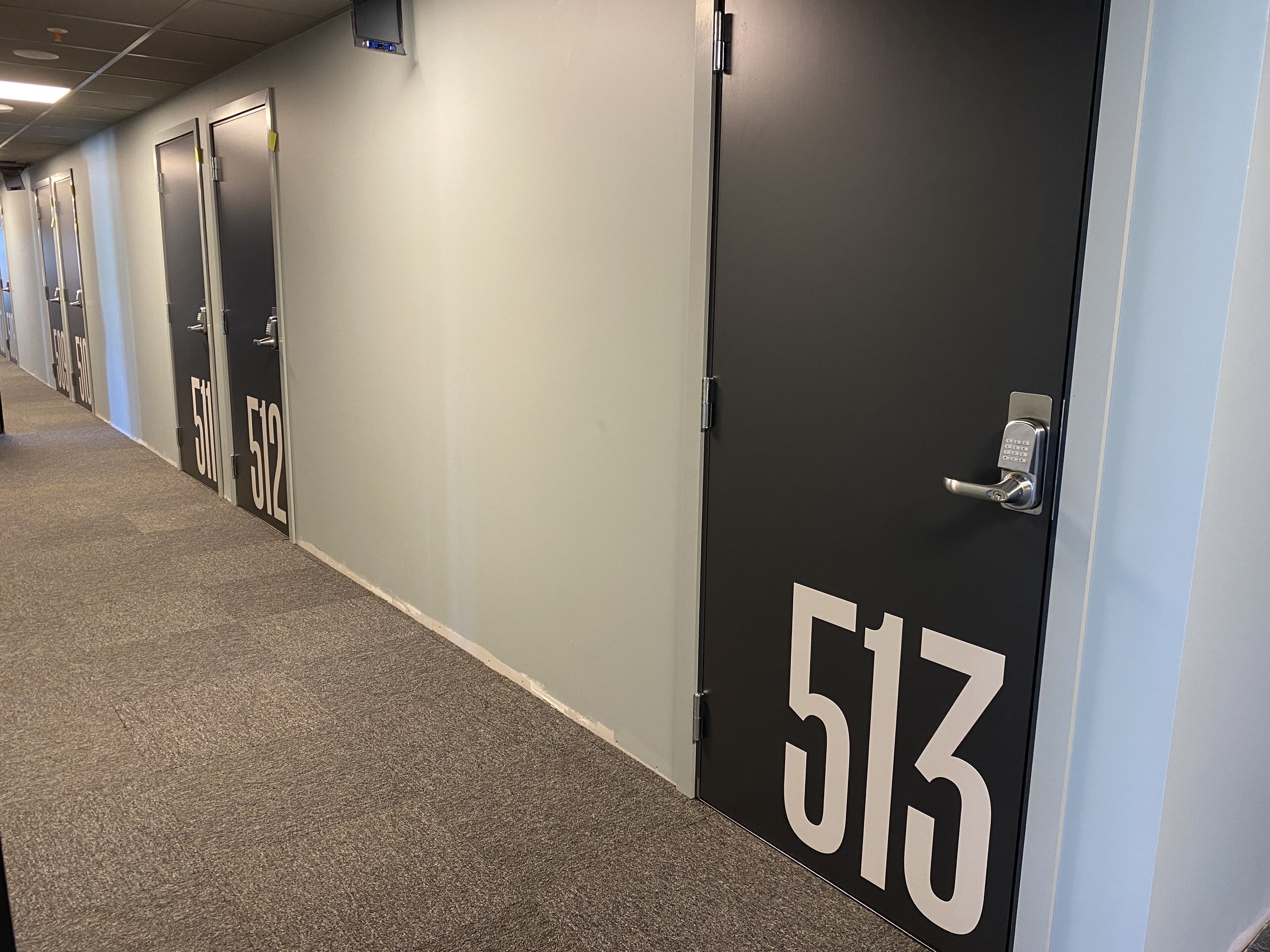 A hallway with doors numbered 511 to 513, carpeted flooring, and a light-colored wall.