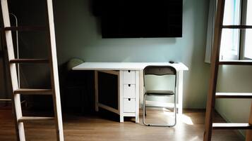 A room with a white desk, a chair, a ladder, and a television mounted on the wall.
