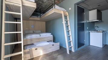 Une pièce compacte comprenant un lit superposé, une échelle, une petite kitchenette et une porte donnant sur une autre pièce.