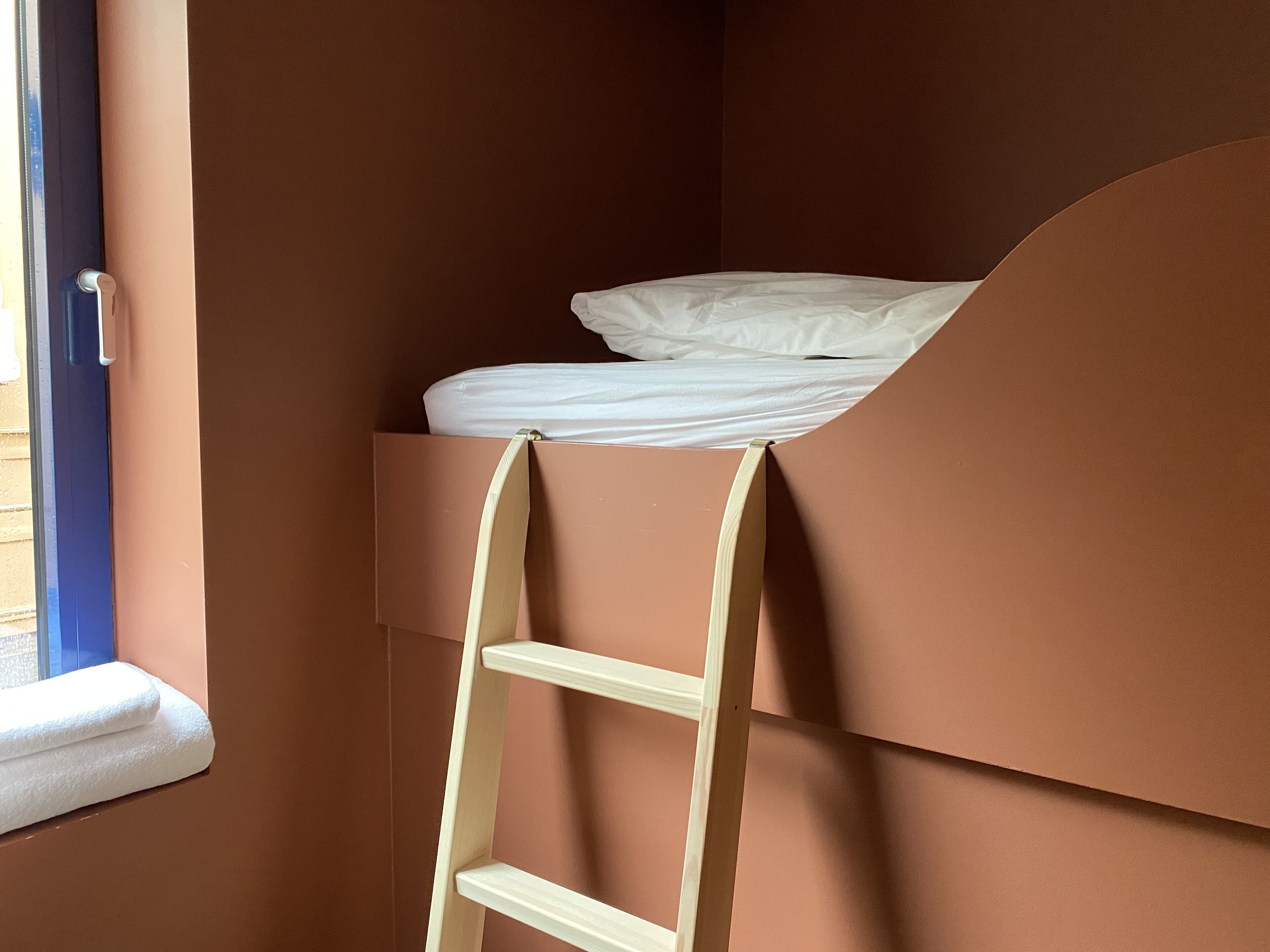 A bunk bed with a ladder, a window, and a door.
