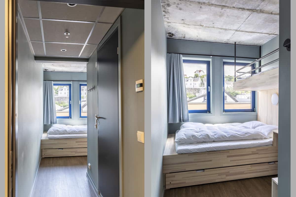 Quarto moderno com beliche, uma janela grande com cortinas e vista para edifícios.