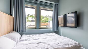 A bedroom with a bed, a window with curtains, and a TV mounted on the wall.
