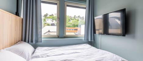 A bedroom with a bed, a window with curtains, and a TV mounted on the wall.