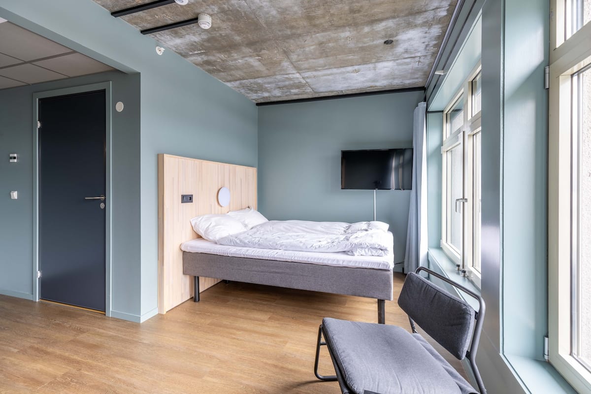 Quarto moderno com cama, um banco, televisão e janela.