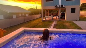 A swimming pool with a person in it, a house with two air conditioning units, and a sunset in the background. - 6 min walk to beach / private pool/ AC (Cabo Rojo)