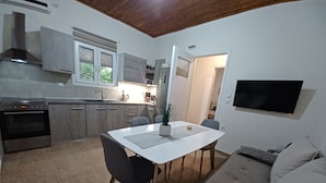Una cocina funcional con electrodomésticos modernos, un comedor con mesa y sillas blancas, y una sala de estar con sofá y televisor montado en la pared.