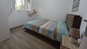 Un dormitorio con cama, cabecera de madera, lámpara de noche, ventana con vistas y aire acondicionado instalado en la pared.