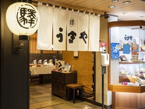 Interior de un restaurante japonés tradicional con suelo de tatami, una barra de madera y una vitrina con productos alimenticios.