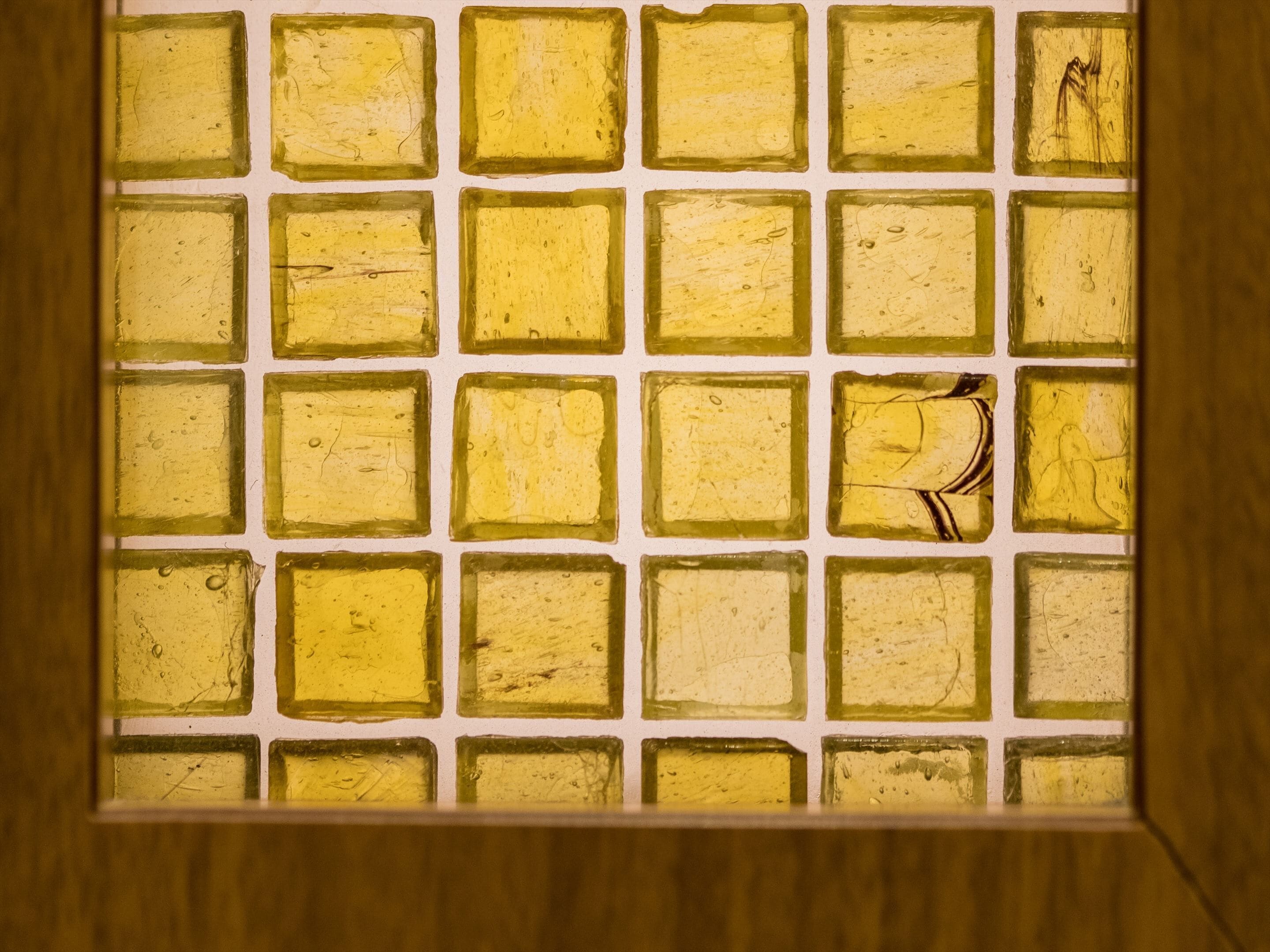 A window with a grid of square panes, each containing a yellowish substance, possibly a type of glass or material.