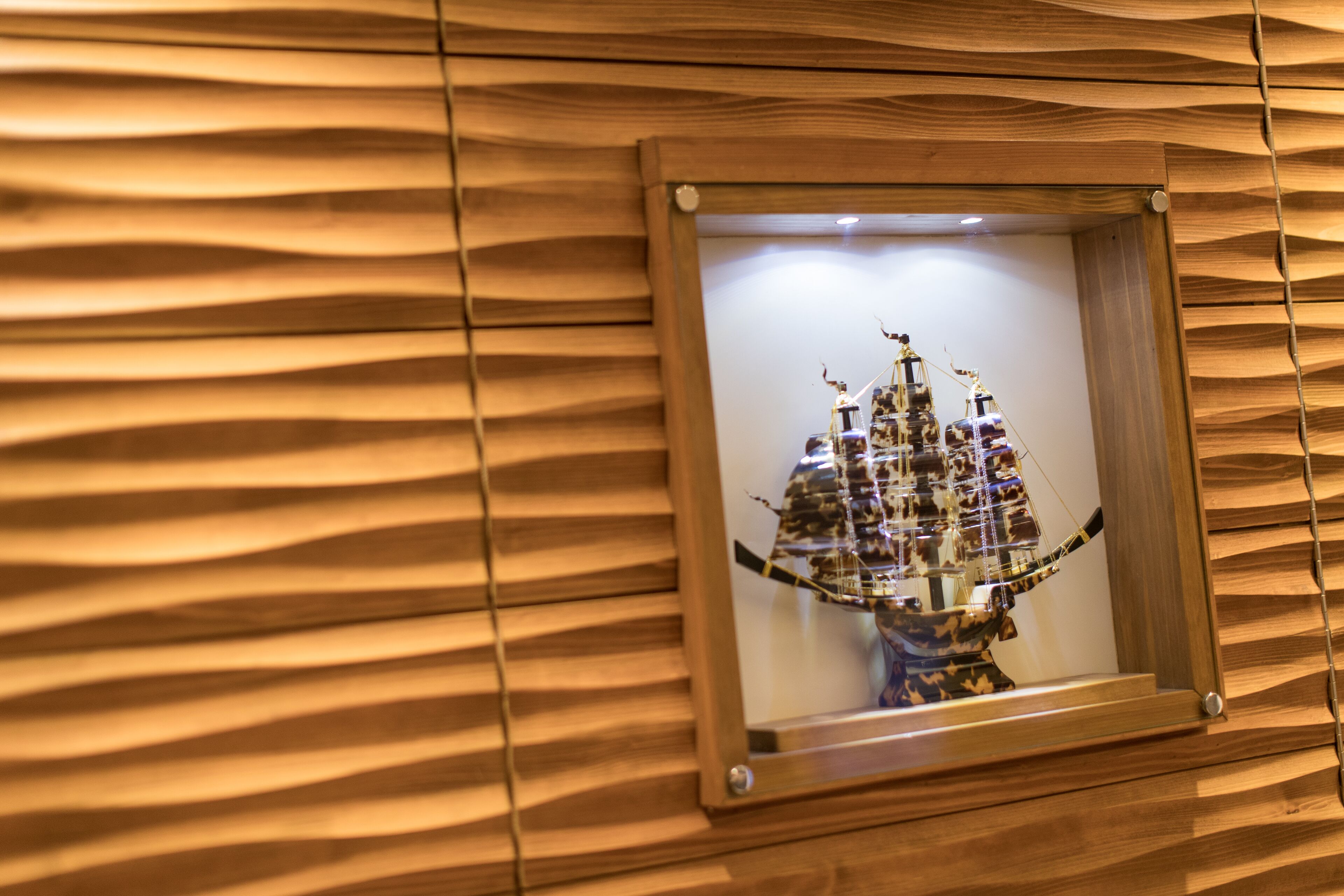 A framed artwork of a ship on a wooden wall with a wavy pattern.