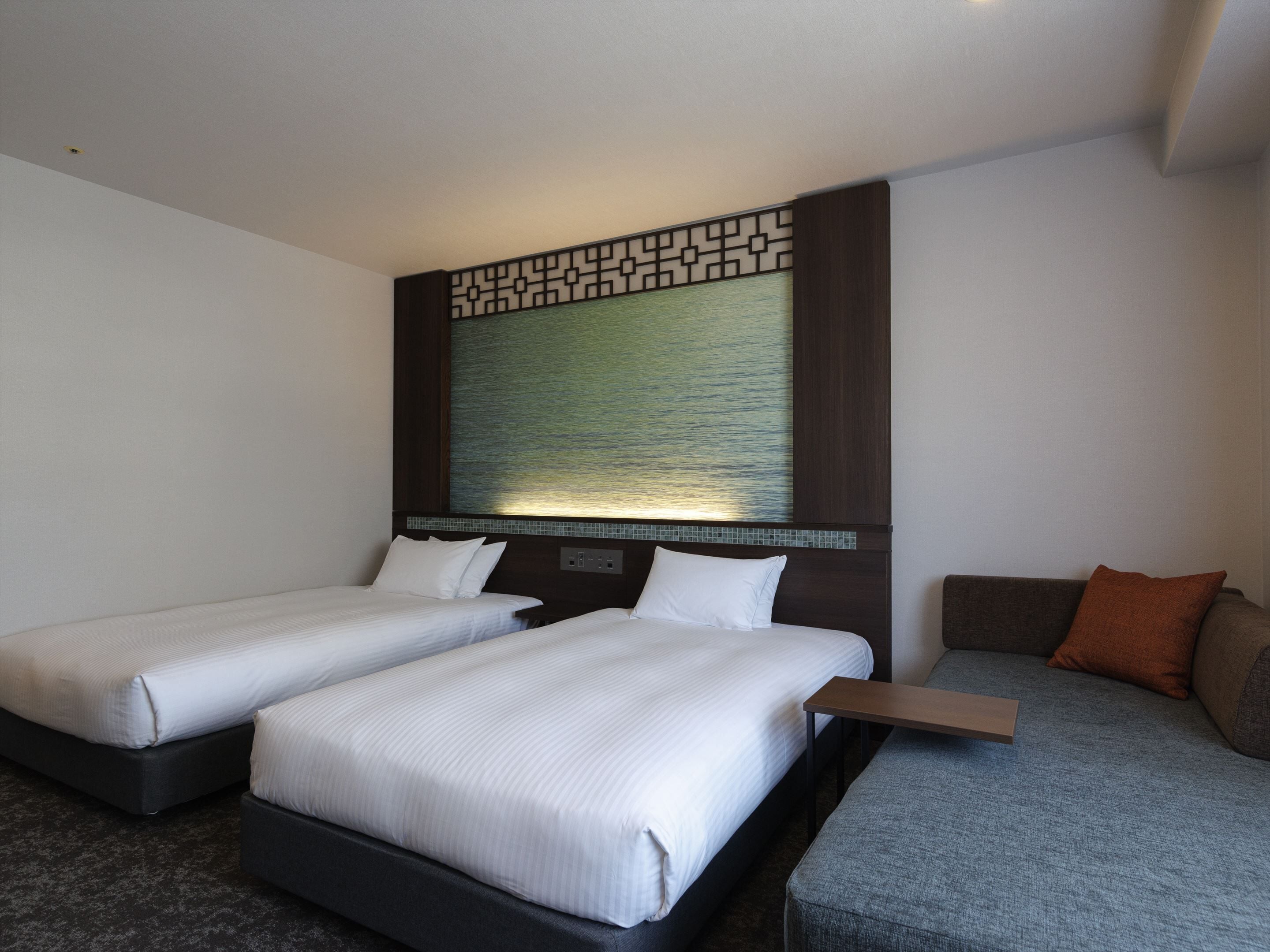 Habitación de hotel con dos camas individuales, un sofá y una mesita.
