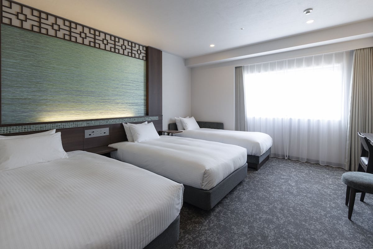 Habitación de hotel con dos camas, un ventanal con cortinas, una obra de arte colgada en la pared y piso alfombrado.