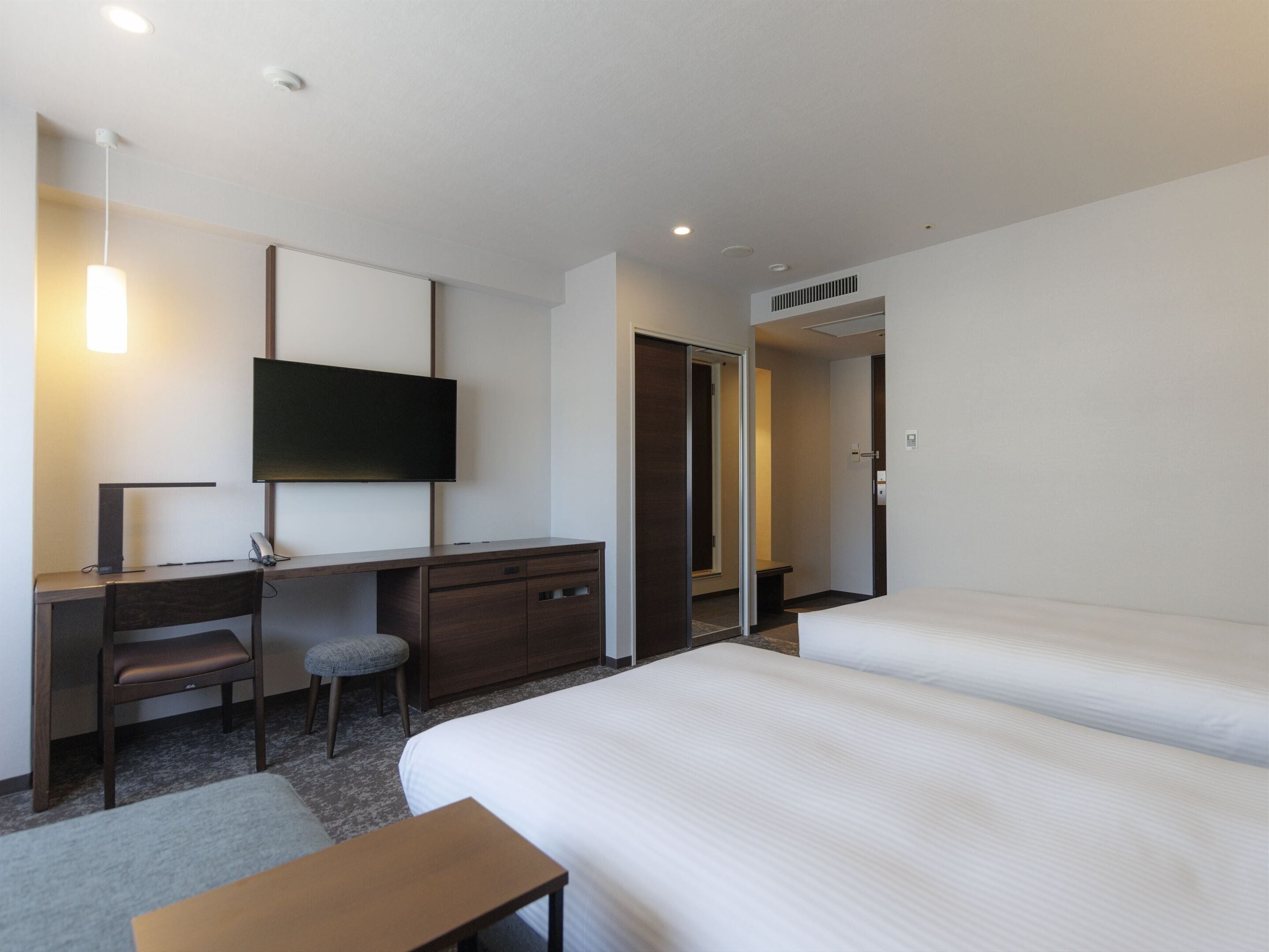 A hotel room with a bed, a desk, a chair, a TV, and a wardrobe.
