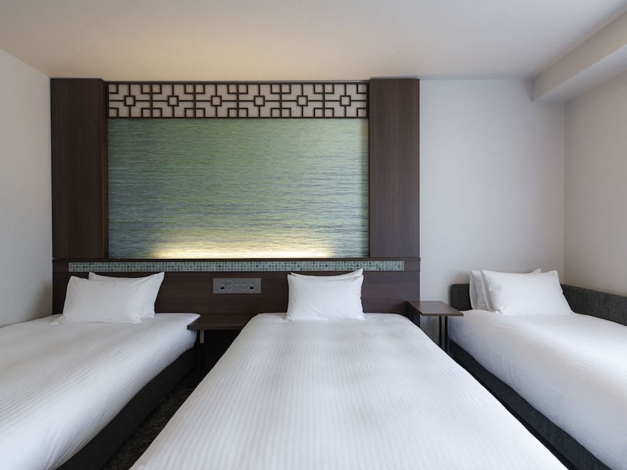 A hotel room with two single beds, a large decorative wall panel, and a small bedside table.