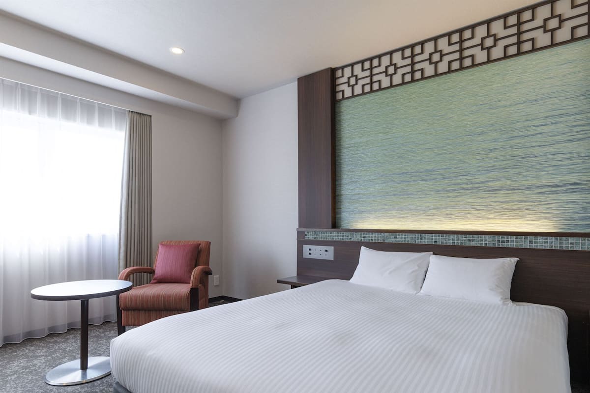 Una habitación de hotel con una cama grande, una silla, una mesita pequeña y un panel decorativo en la pared.