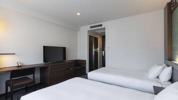 Habitación de hotel con dos camas, un escritorio, un televisor y una puerta que da a un baño.