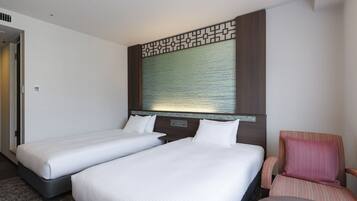 A hotel room with two single beds, a small seating area with a chair, and a decorative wall panel above the beds.