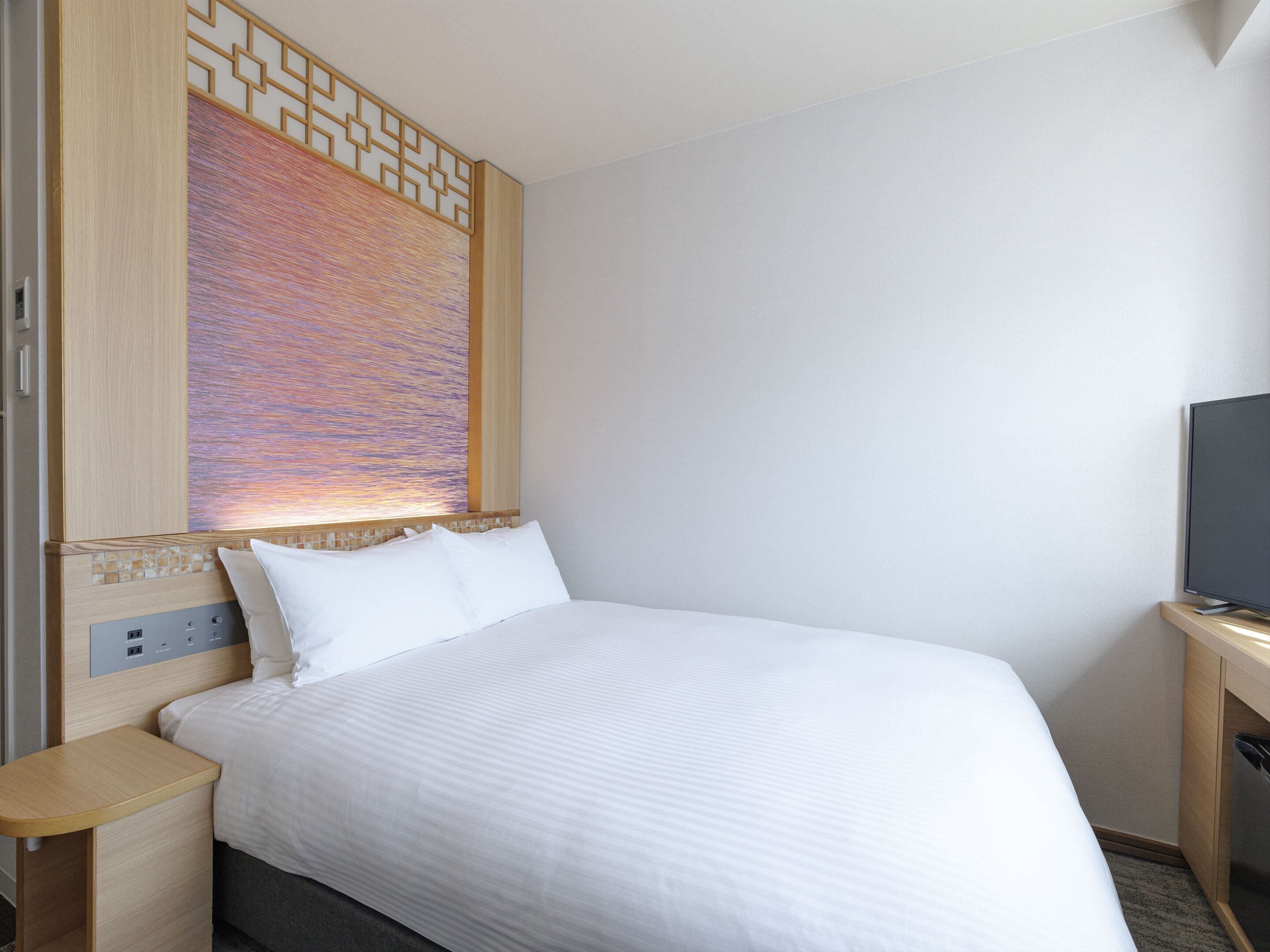 A hotel room with a bed, a TV, and a decorative wall panel.