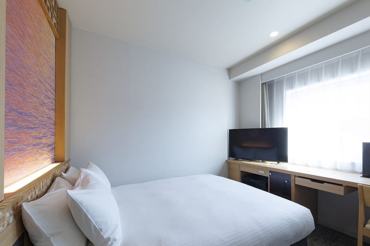 Una habitación de hotel con una cama, televisión y ventana con cortinas.