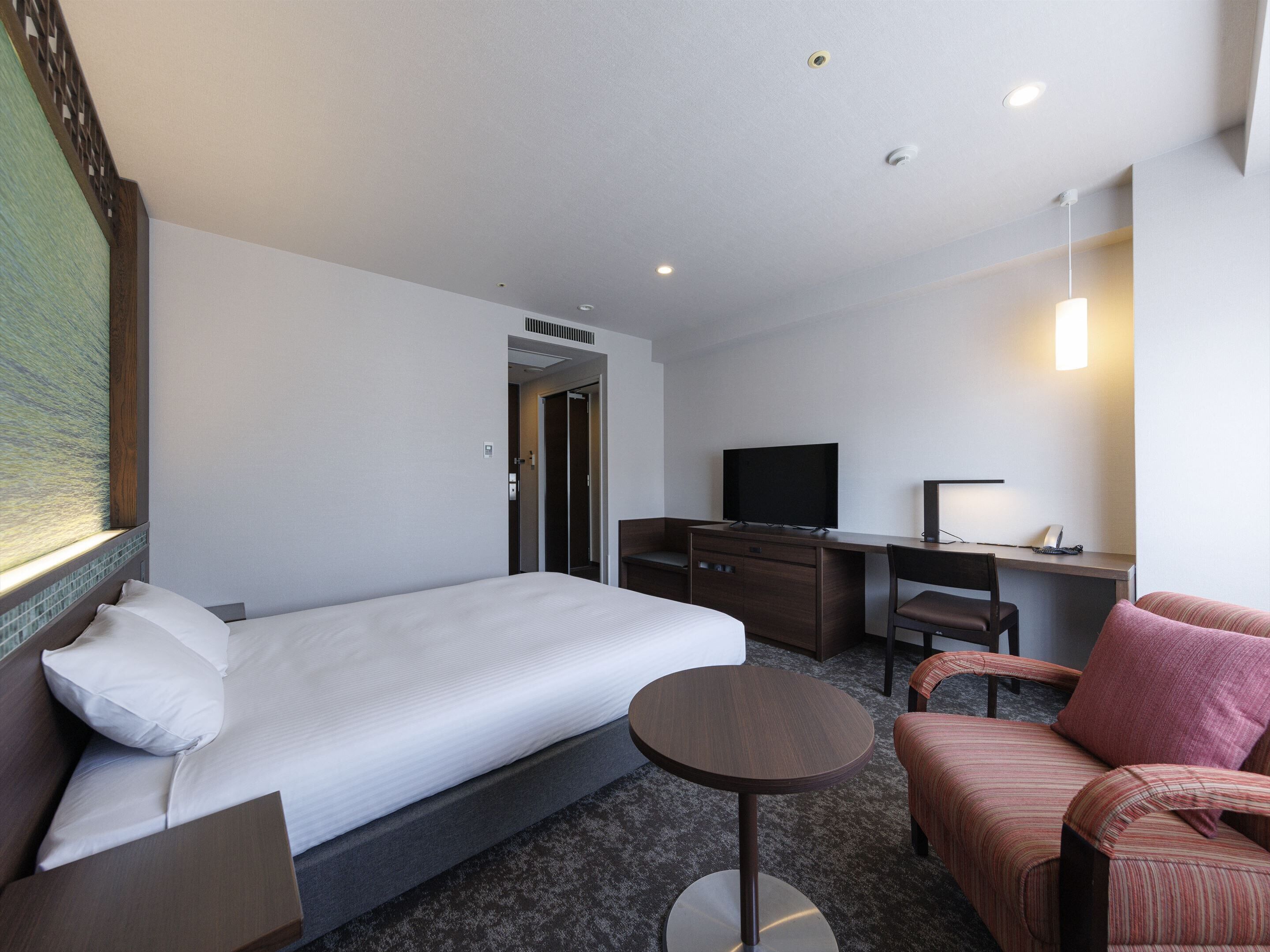 A hotel room with a bed, a desk, a television, a chair, and a small table.