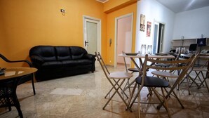 A living room with a black sofa, a dining table with chairs, and a kitchen area with a laptop and glassware. - LA DIMORA DEL PRINCIPE (Trapani)