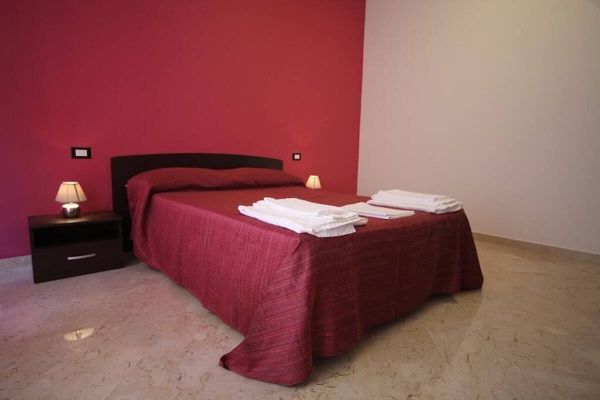 Uma cama de solteiro com um cobre-leito vermelho, duas luminárias de cabeceira e uma mesa de cabeceira com abajur.