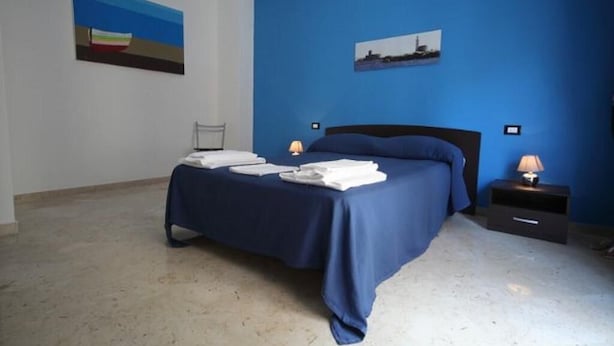 A bedroom with a bed, a nightstand, a chair, and artwork on the walls. - LA DIMORA DEL PRINCIPE (Trapani)