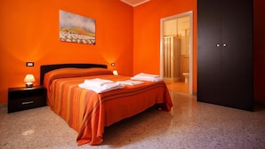 A hotel room with an orange wall, a bed with striped bedding, a nightstand with a lamp, and a painting above the bed. - LA DIMORA DEL PRINCIPE (Trapani)