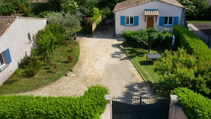 A residential area with a house featuring a tiled roof, a gravel driveway, and a small garden with various plants and flowers.