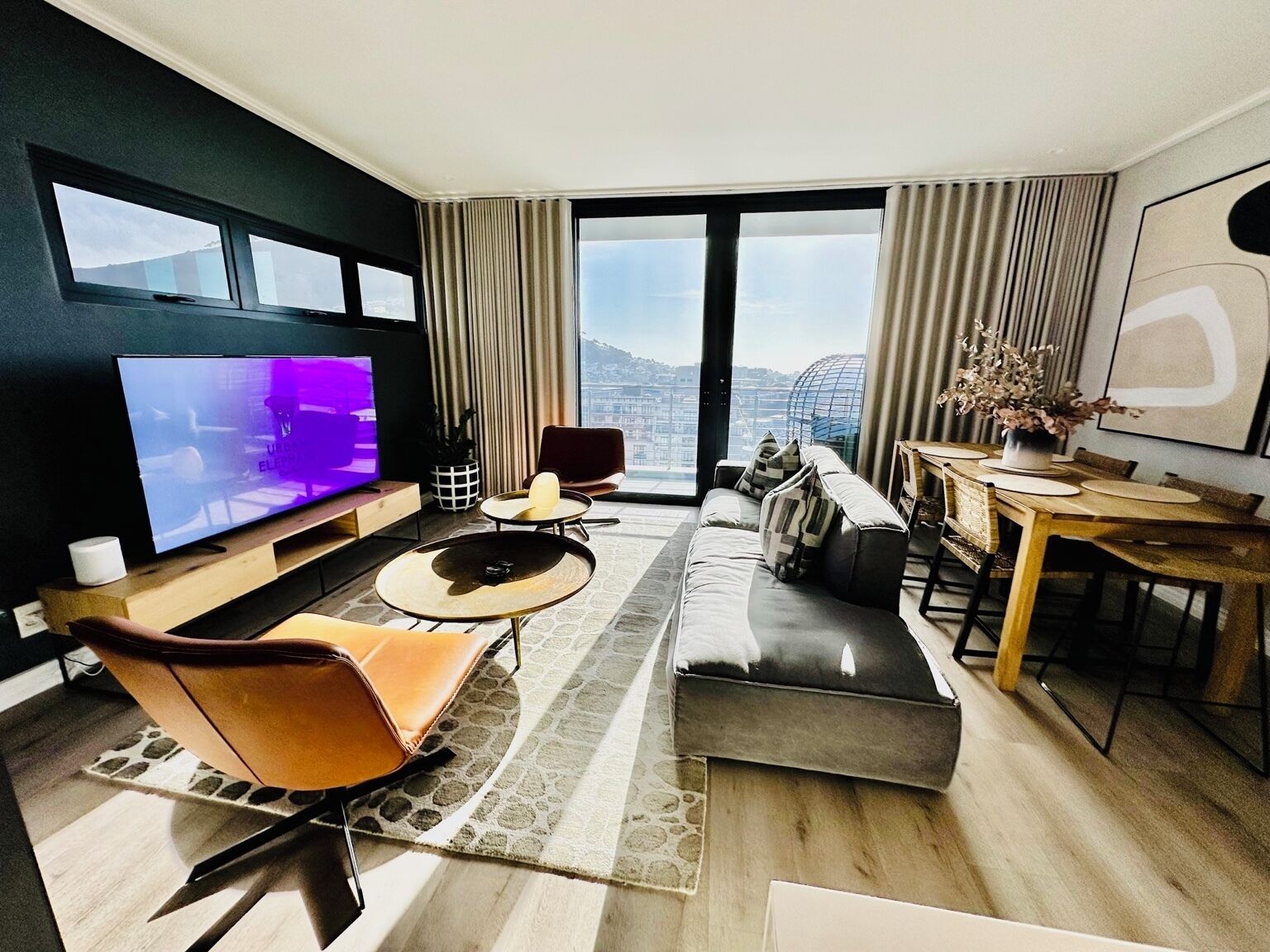 Una sala de estar moderna con un televisor de pantalla plana, un sofá, una mesa de comedor y vistas a la ciudad.