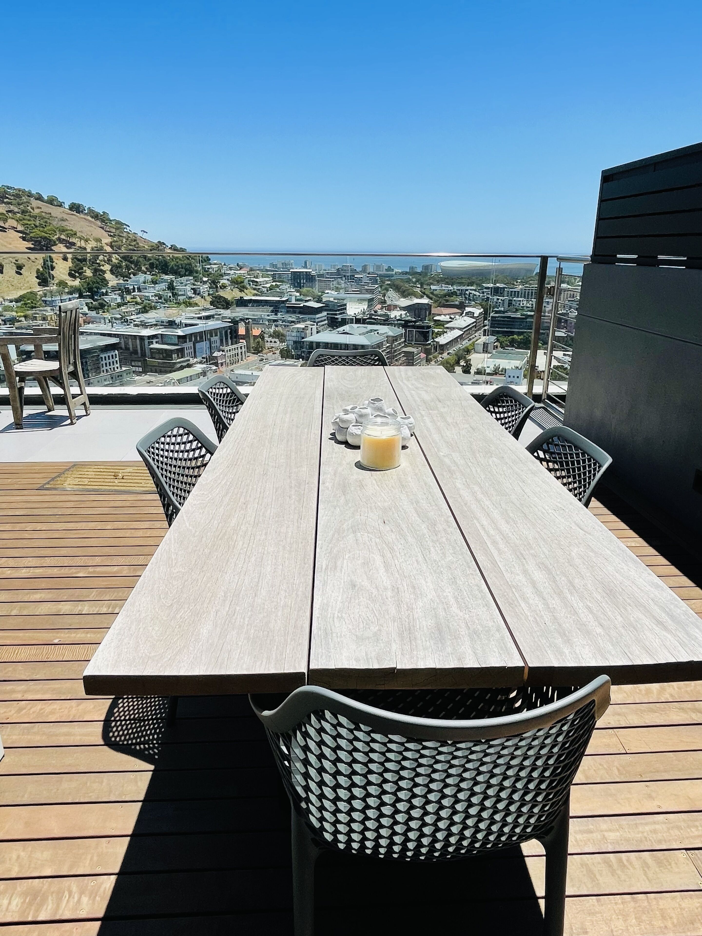 Um deck de madeira com mesa e cadeiras, com vista para um horizonte urbano e colinas.