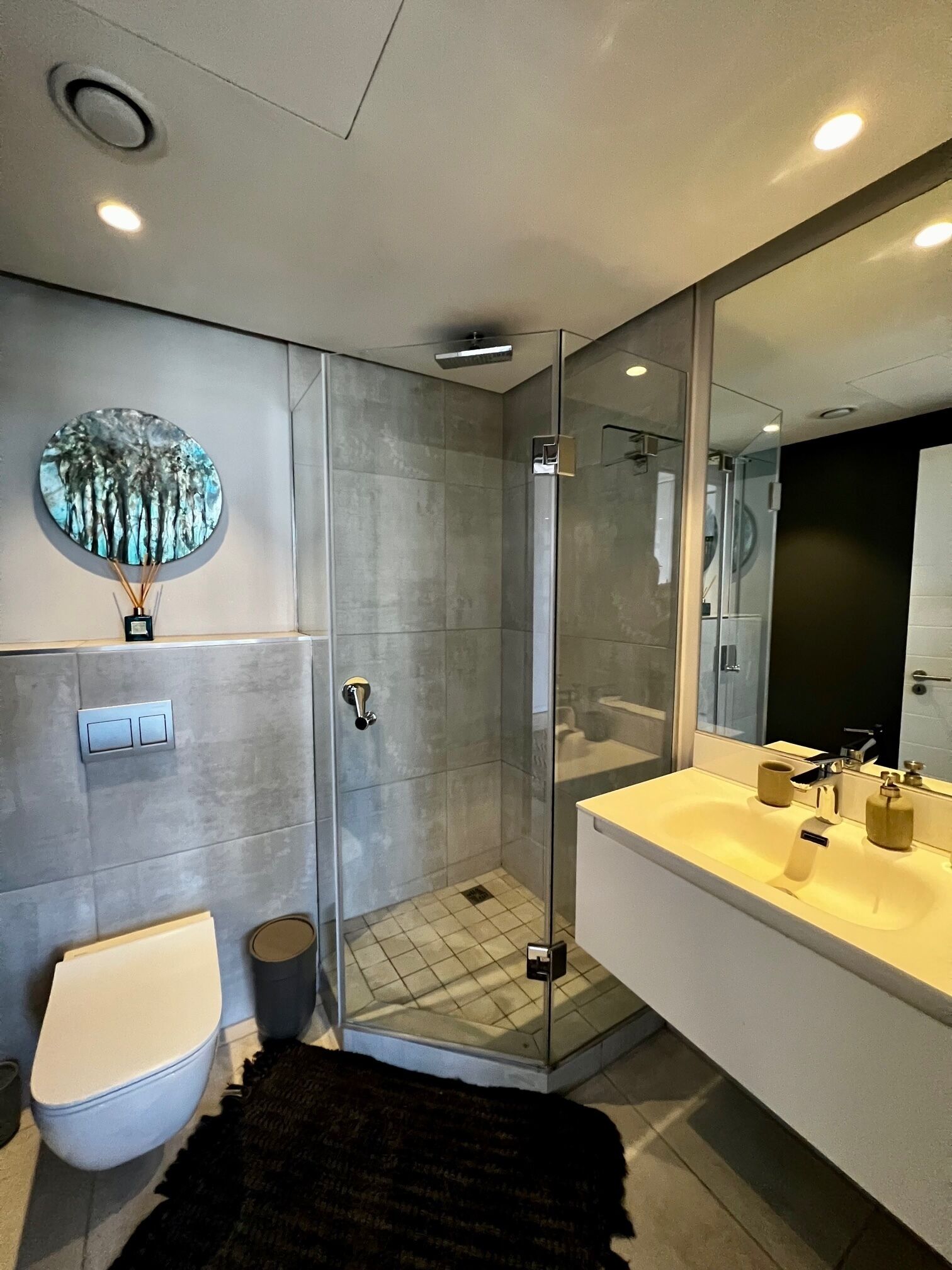A modern bathroom with a glass-enclosed shower, a white toilet, and a large mirror above the sink.