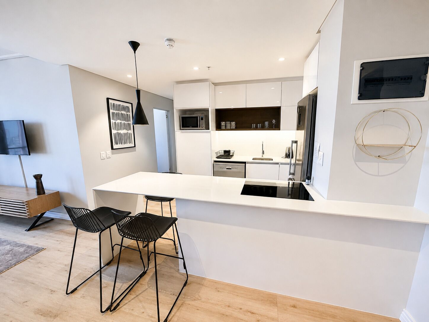 A modern kitchen with white cabinetry, a black countertop, and two black bar stools.