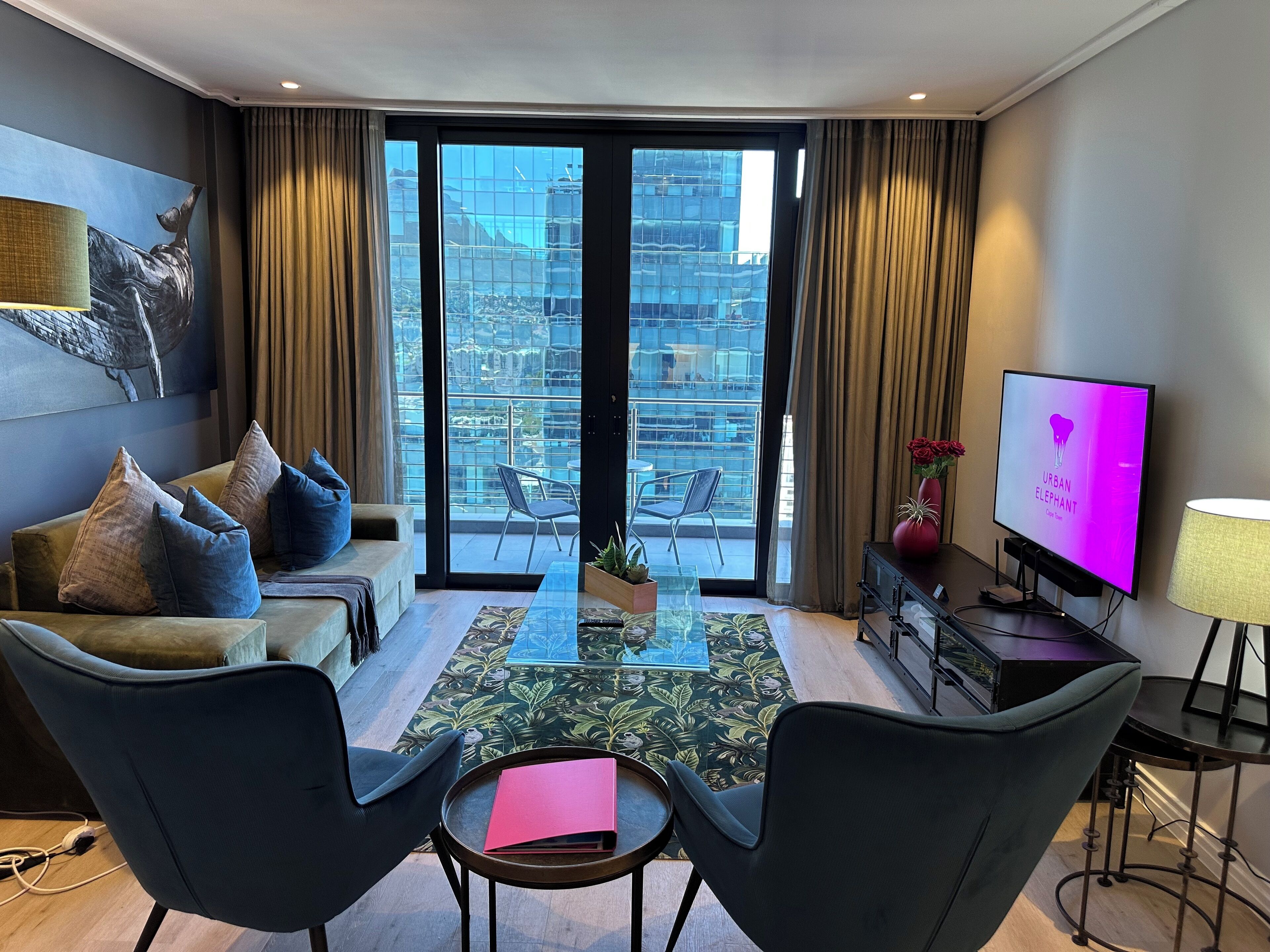 Un salon moderne comprenant un canapé, deux fauteuils, une table basse, un téléviseur et un balcon offrant une vue sur la ville.