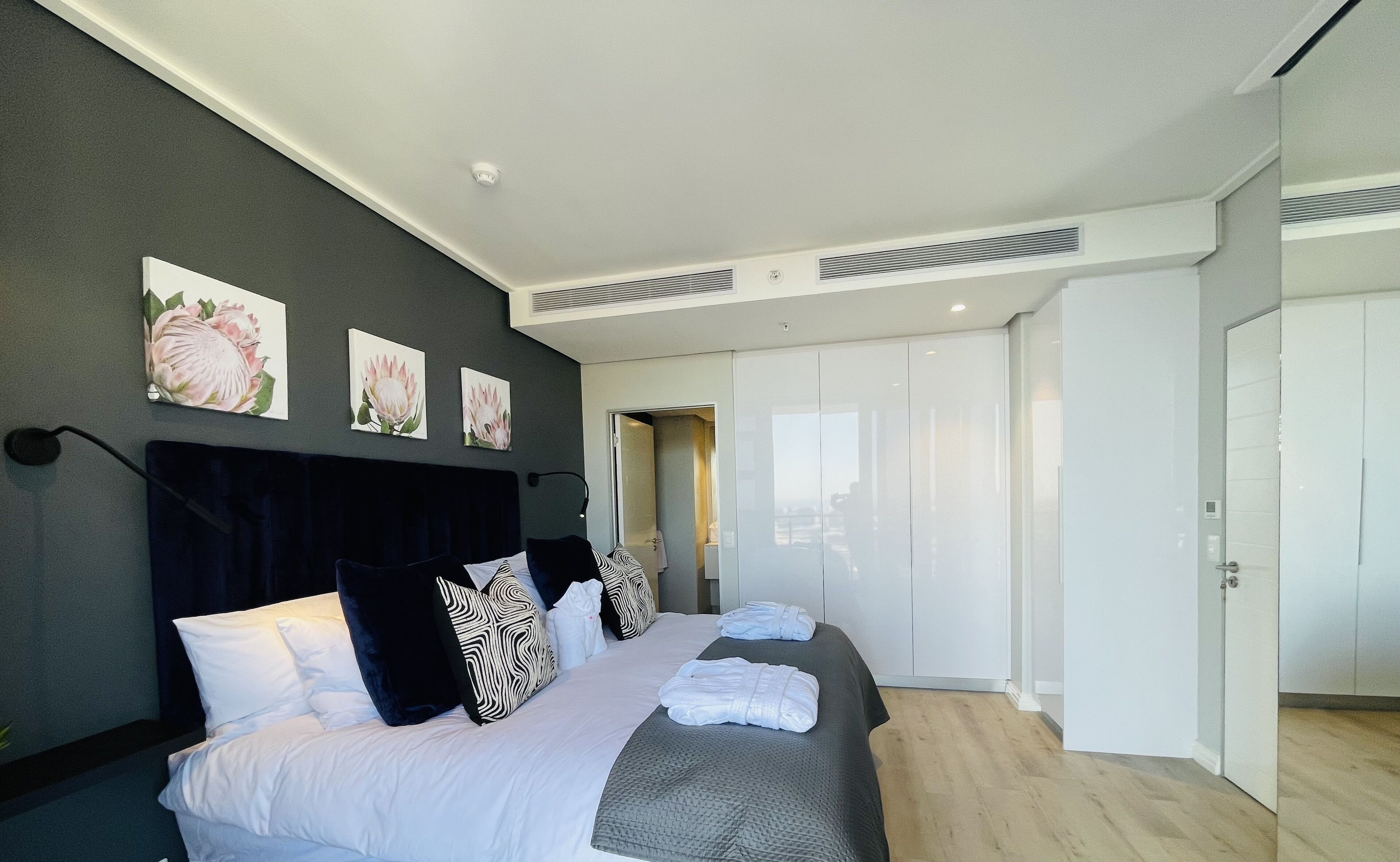 A modern hotel room with a large bed, dark headboard, and artwork on the wall.