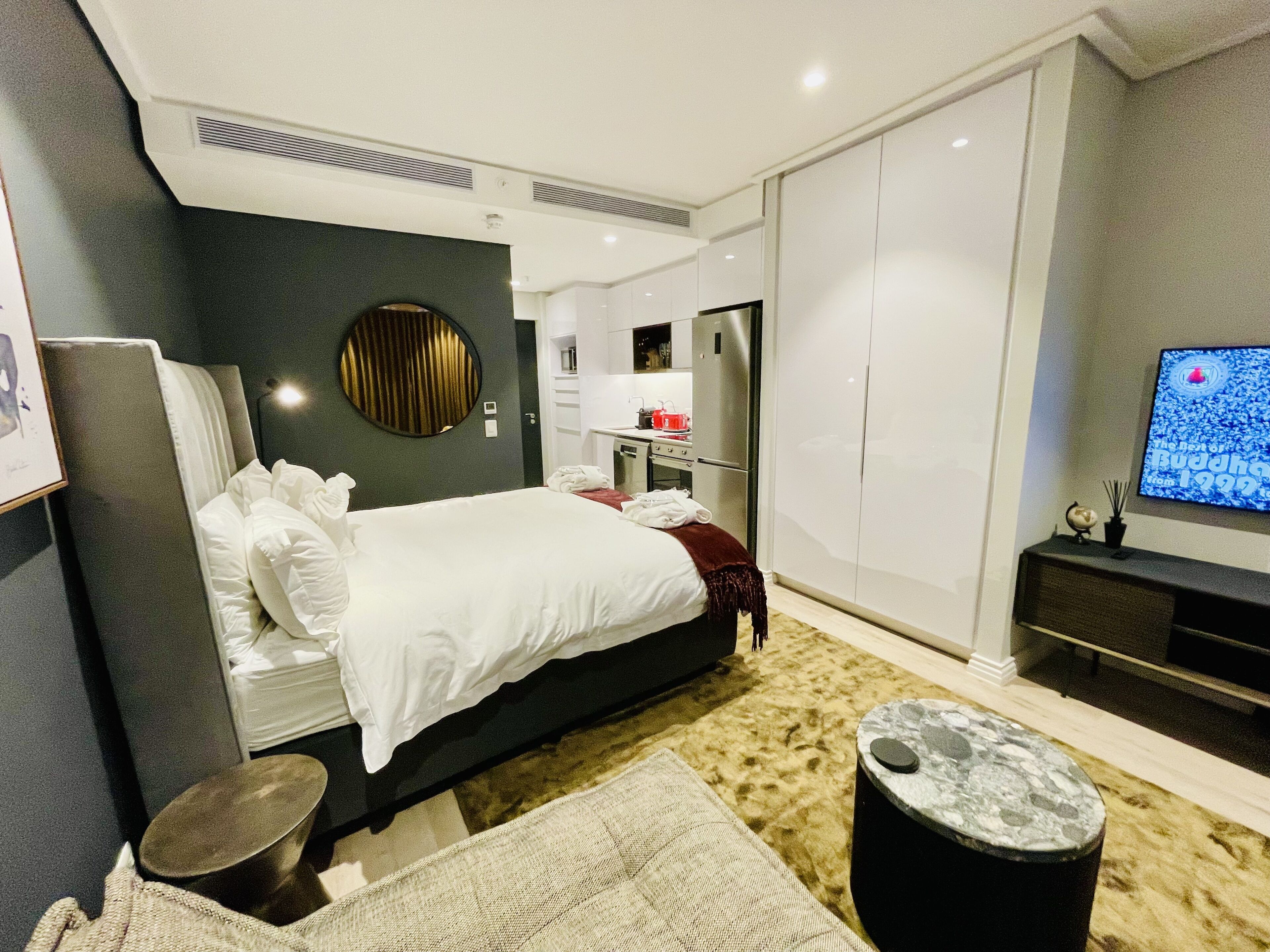 Una habitación de hotel moderna con una cama grande, televisión, armario y kitchenette.